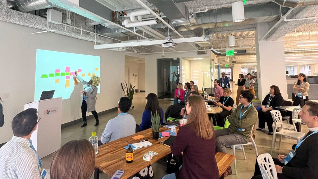 People sat at an innovation workshop while the presenter puts sticky notes on the wall