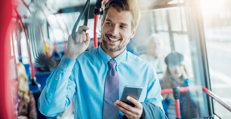 A smiling man in a blue shirt standing on a bus holding his phone