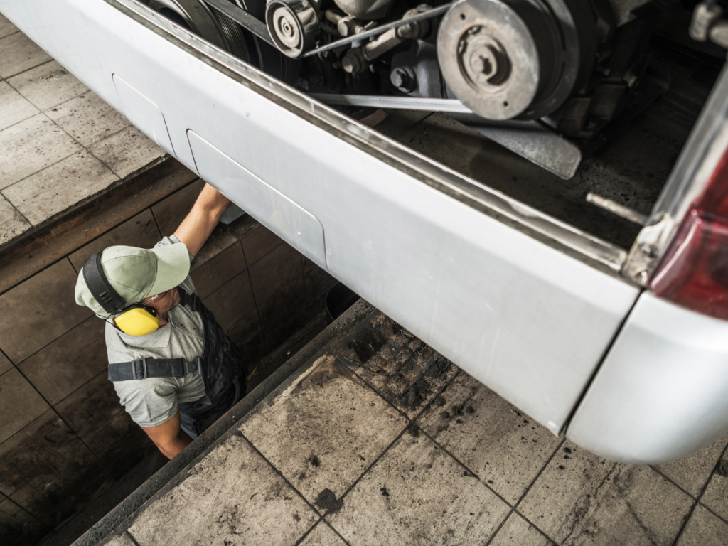 An image of a person inspecting a bus from within a vehicle inspection pit