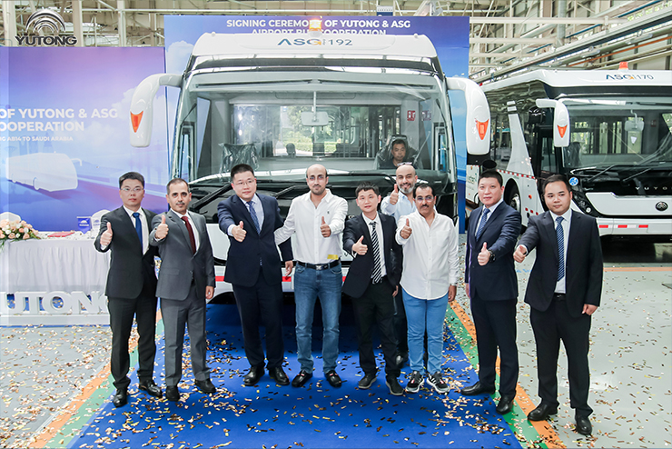 A group of Yutong employees stand in front of a Yutong bus onstage, with their thumbs up