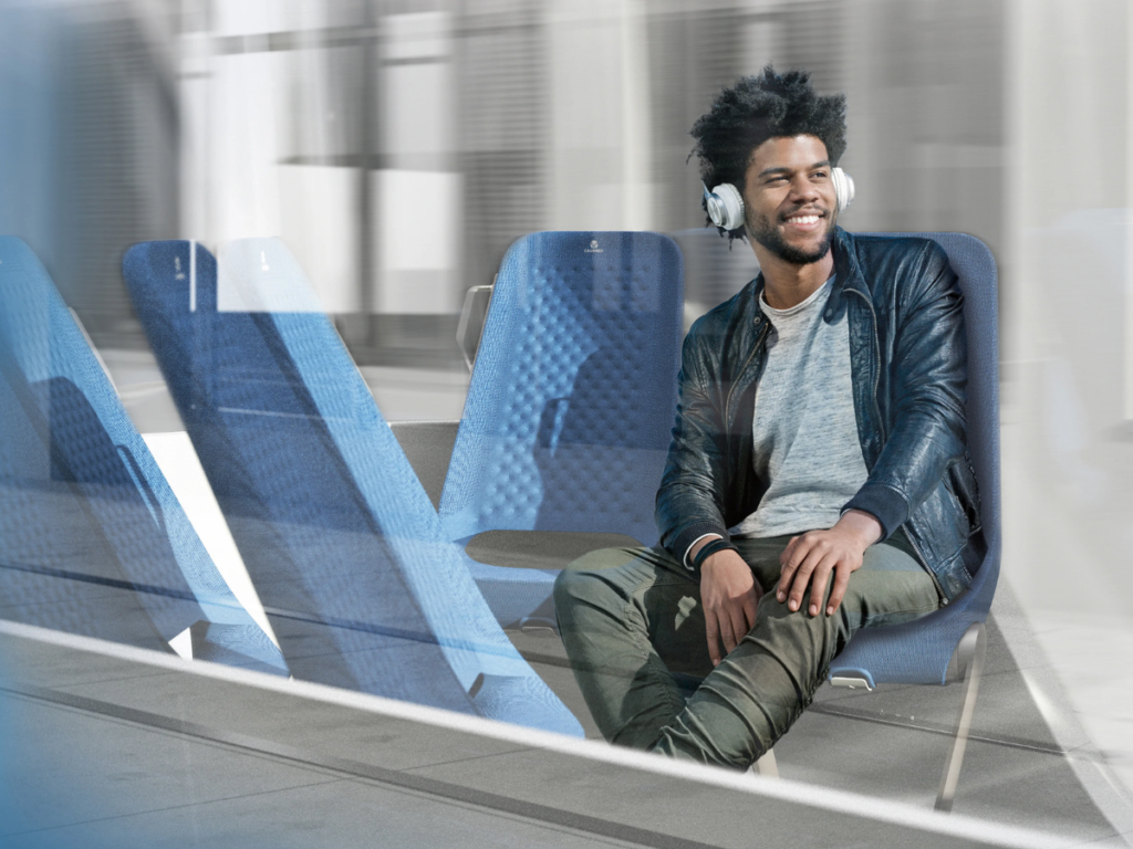 A man wearing headphones smiles while sat on a bus