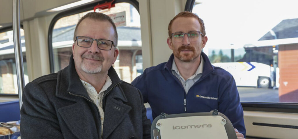 Two men sit on a bus holding an Icomera mobile access router