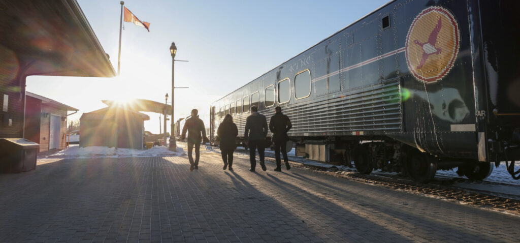 Four people walking past a train car on a sunny day