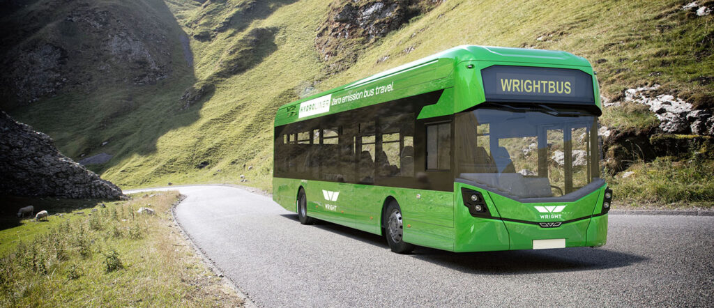A bright green bus travels down a road with tall green hills on either side. The bus has the wrightbus logo on it.