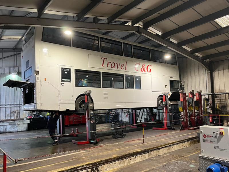 A white double decker bus is being lifted by Totalkare's red vehicle lifts