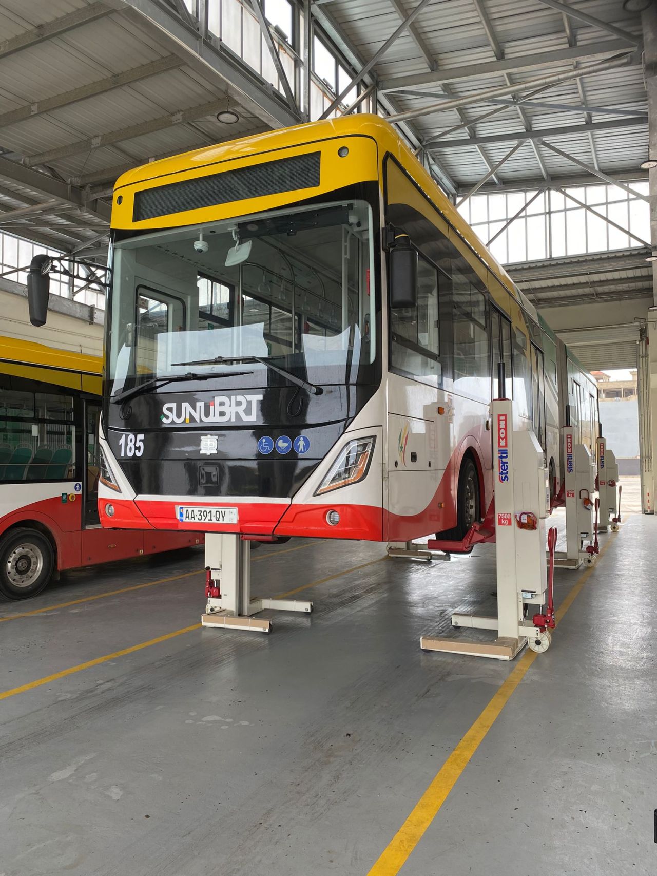 Red and yellow bus suspended in the air by a vehicle lift