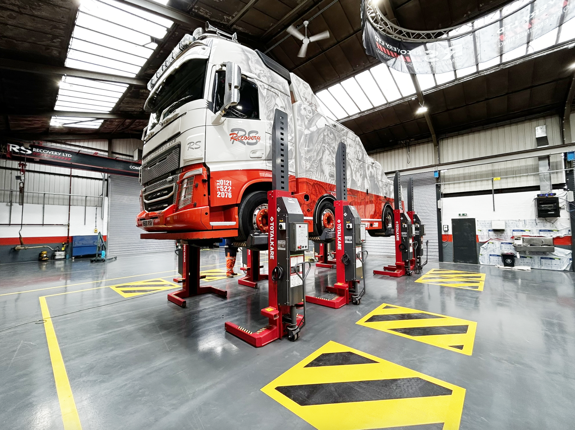 A red and white lorry cabin lifted in mid-air by Totalkare's red mobile column lifts in a maintenance workshop