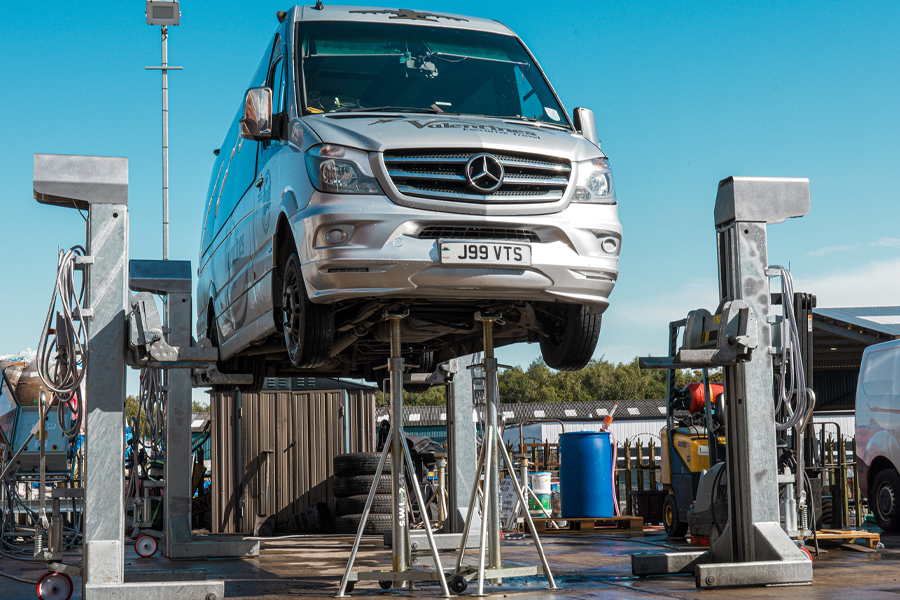 A silver Mercedes-Benz van lifted on a Totalkare washbay mobile column lift, supported by axle stands, in an outdoor maintenance area.