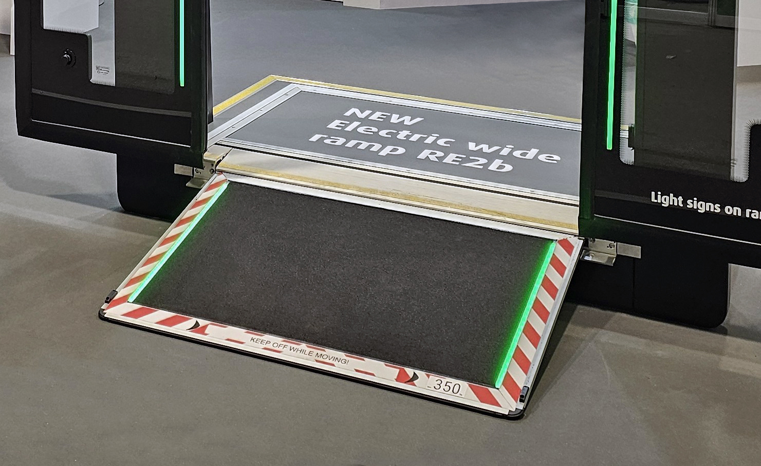 Close-up view of the RE2b electric wide ramp extended from a bus doorway, featuring safety markings and green LED edge lights for improved accessibility.