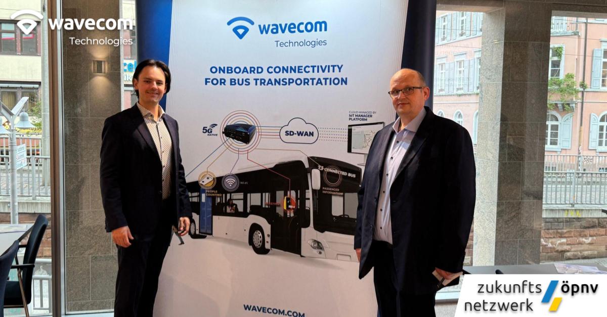 Two men stand beside a Wavecom Technologies display showcasing onboard connectivity solutions for bus transportation, featuring technologies like 5G, SD-WAN, and IoT management, at a public transport networking event.