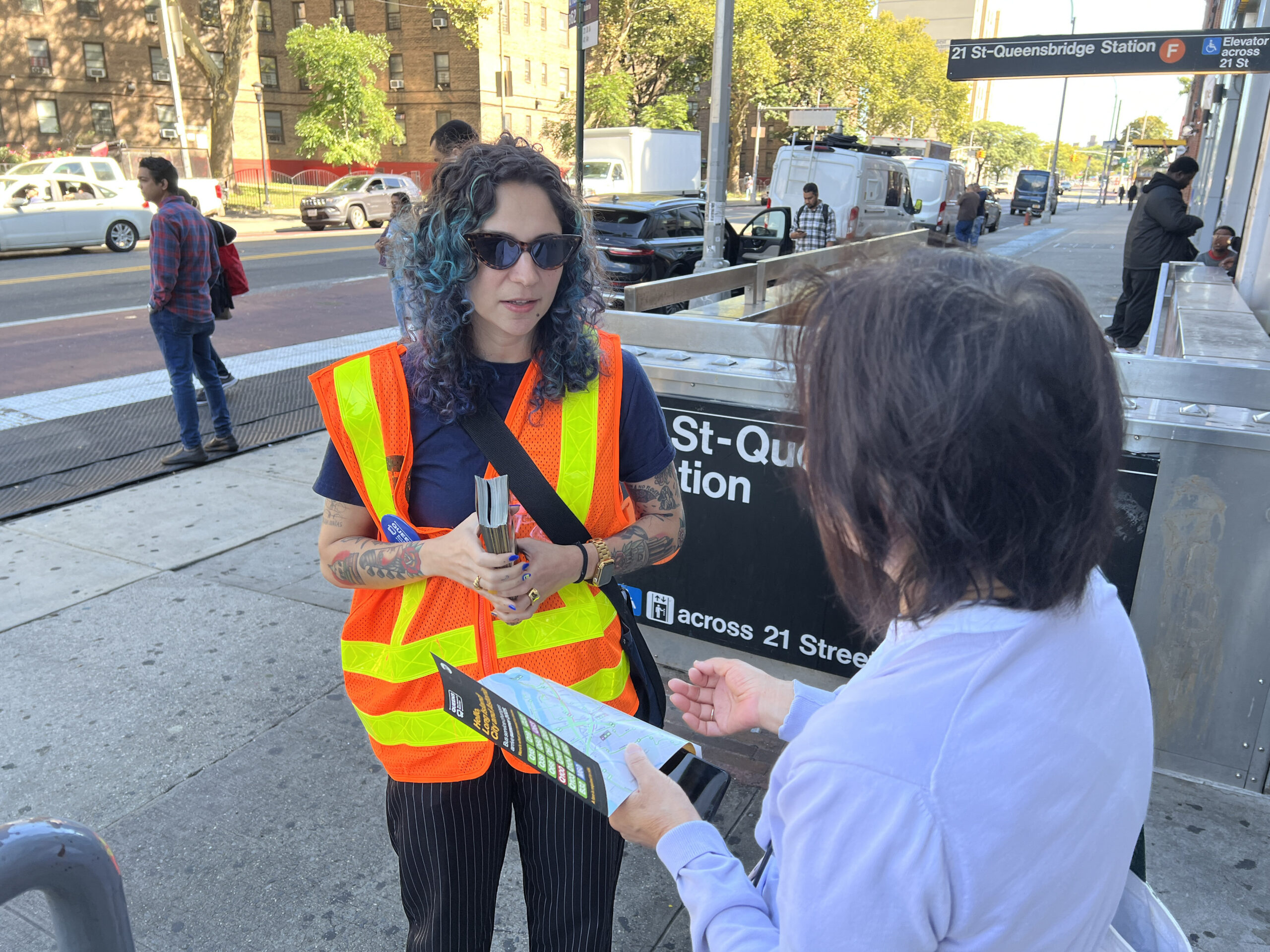 Two people conversing on a sidewalk, one in a high-vis jacket