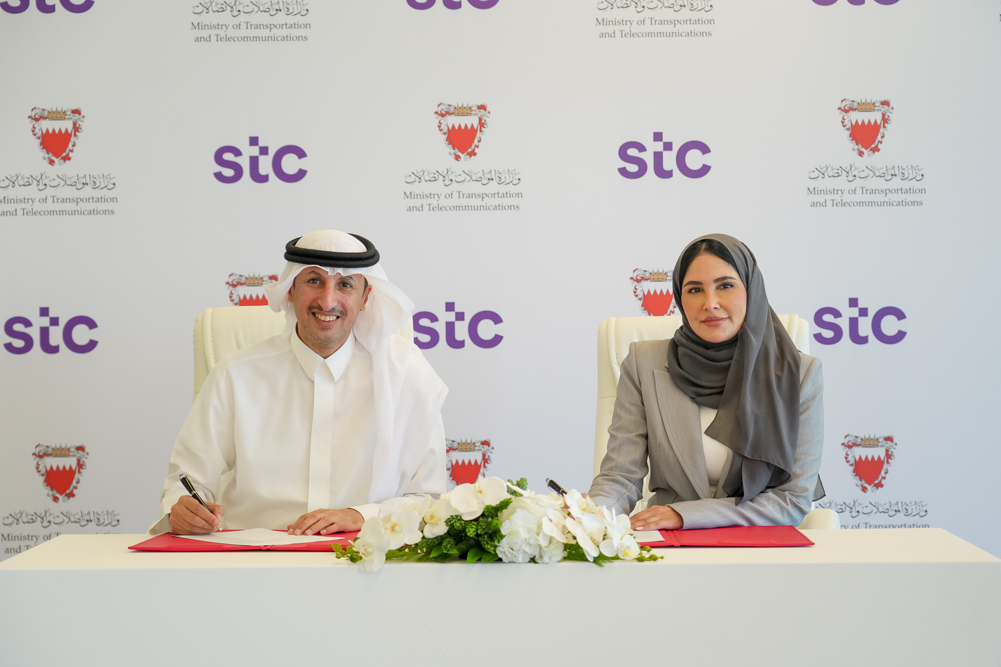 Two people smiling at the camera as they sign a contract