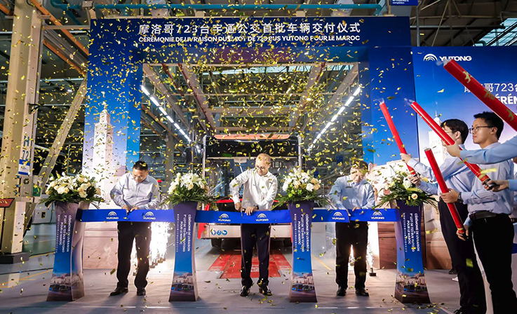A group of people cutting a ribbon at a bus factory as celebrations commence with confetti