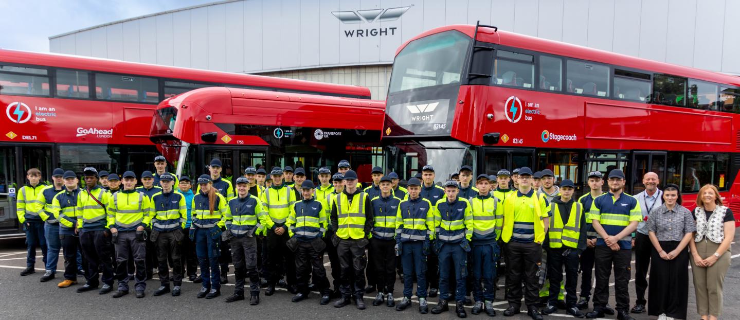 A large group of young people stood in front of bright red buses