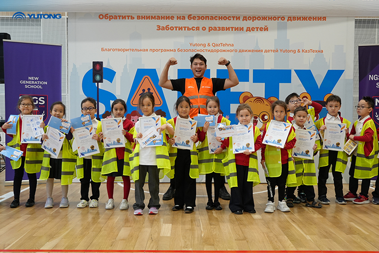A group of children with certificates, and a man posing with a high-visibility jacket behind