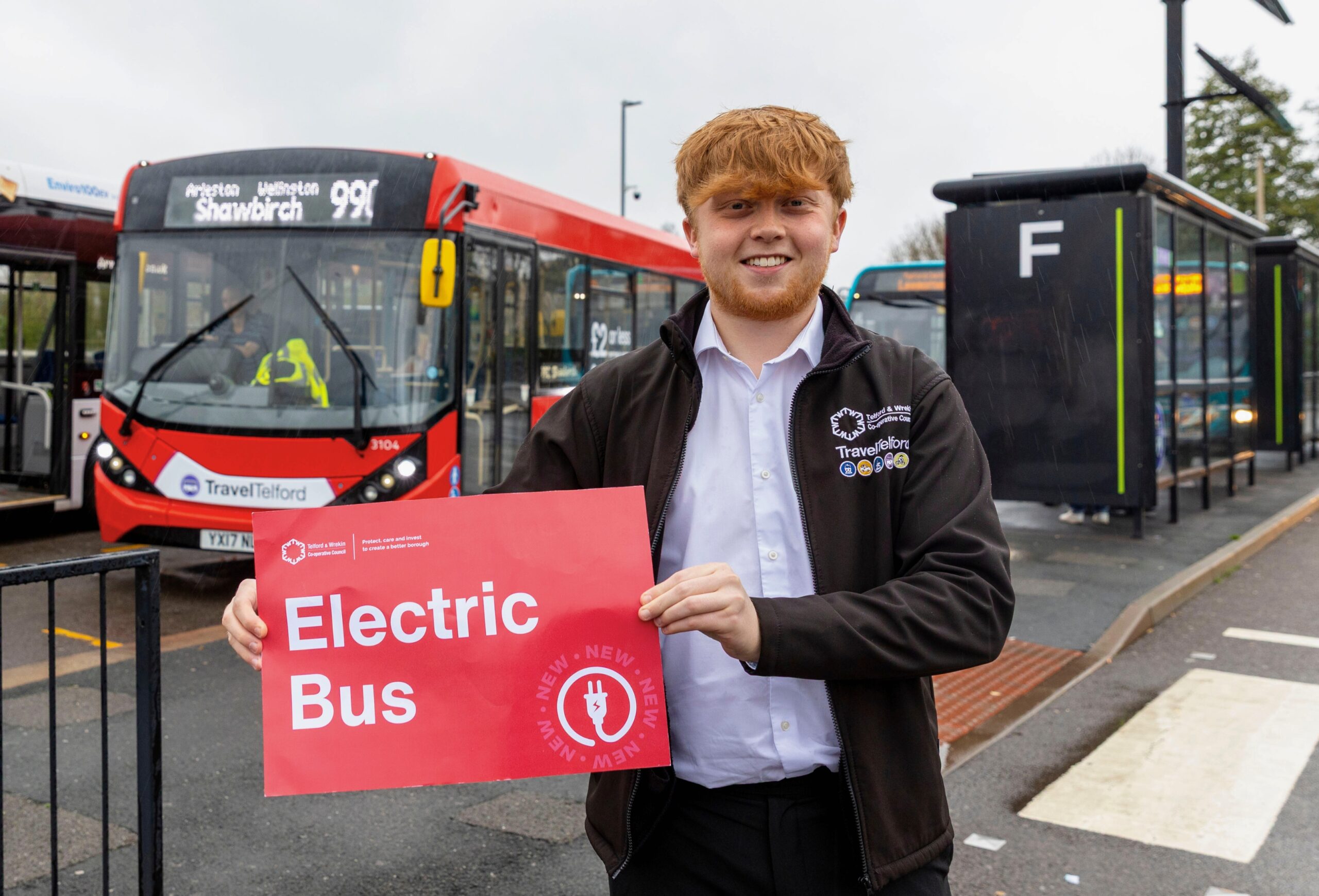 A man holding up a red sign saying Electric Bus whilst stood in front of said bus