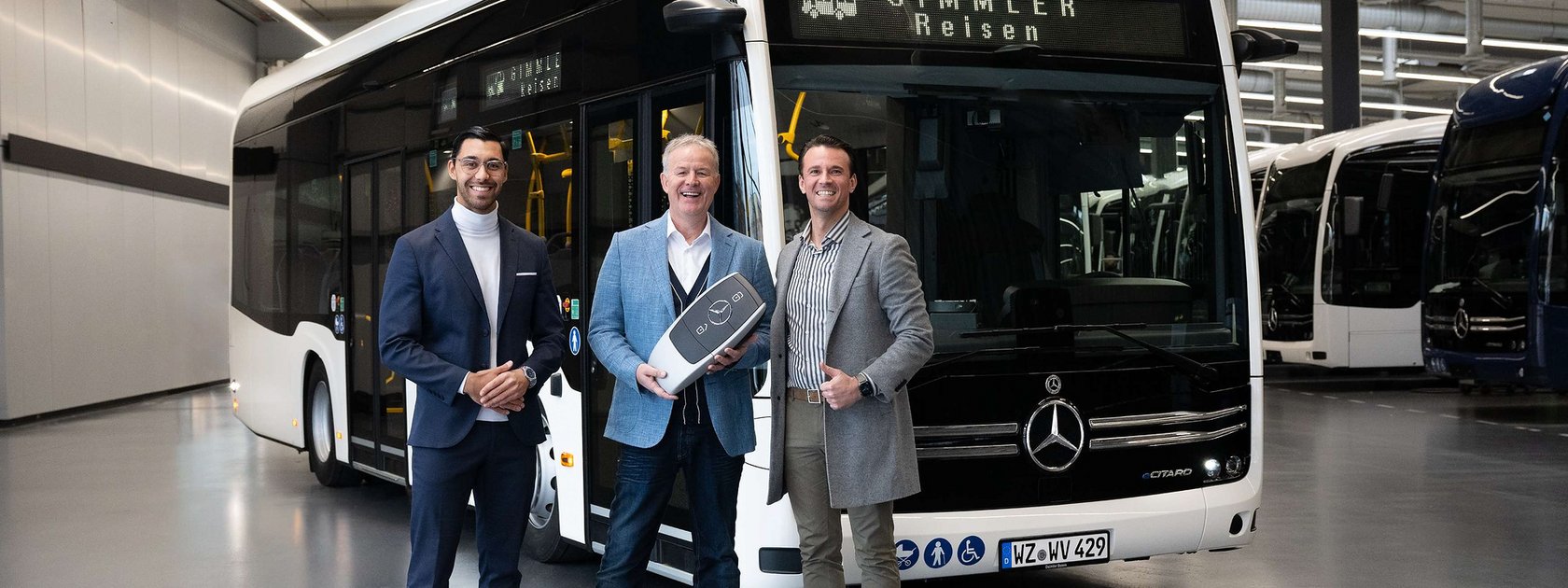 Two men smiling in front of a bus, one holding an absolutely massive novelty key