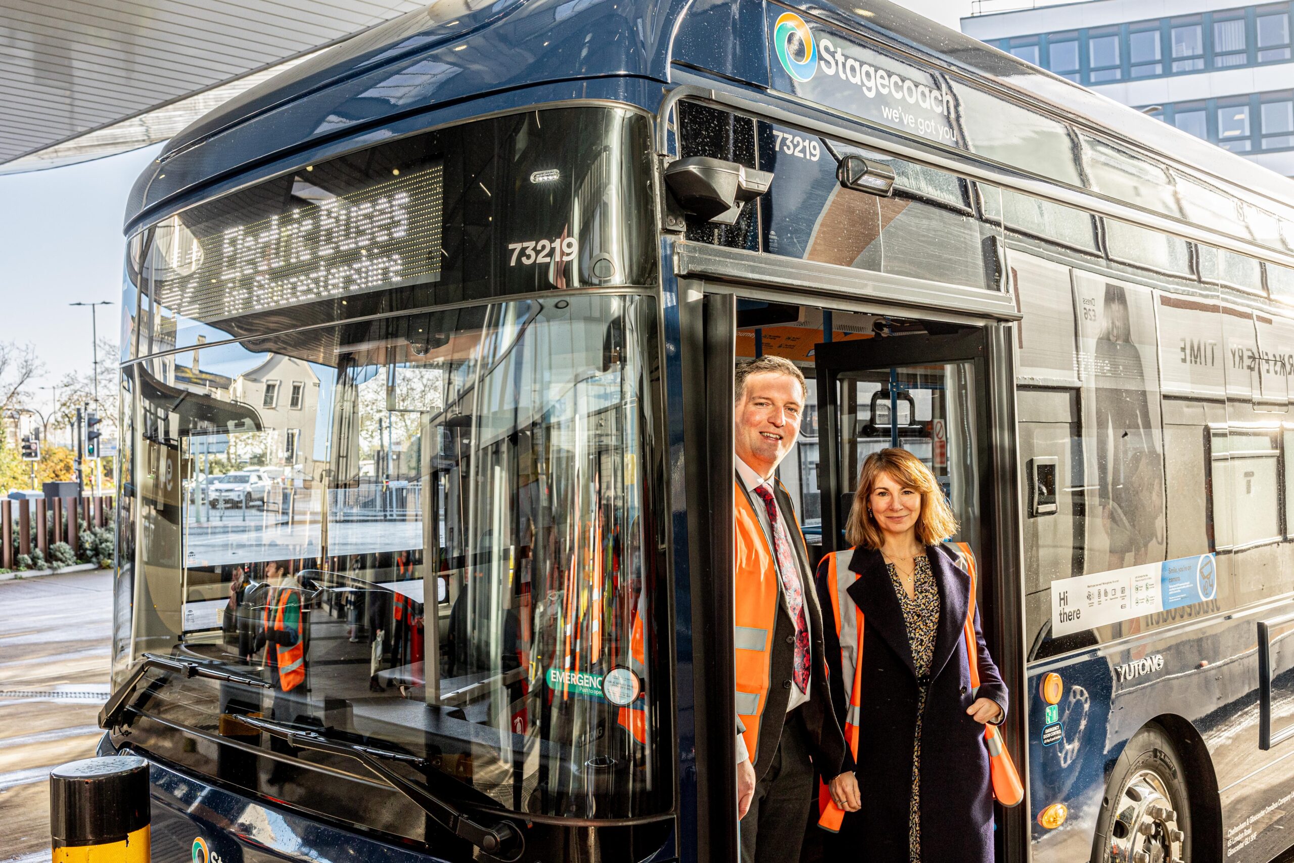 Two people smiling as they stand in the doorway of a shiny bus