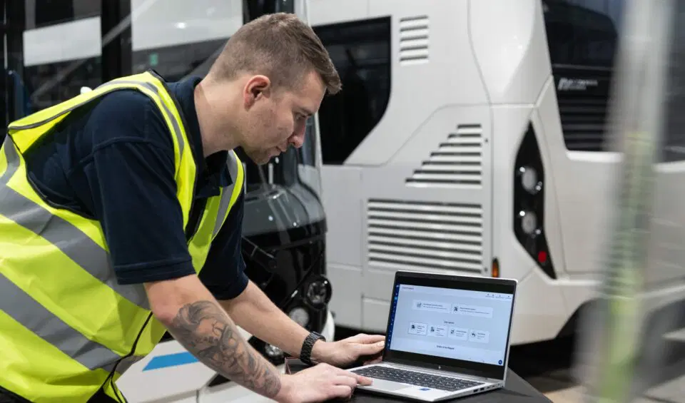 A man checking some software on a laptop by a bus