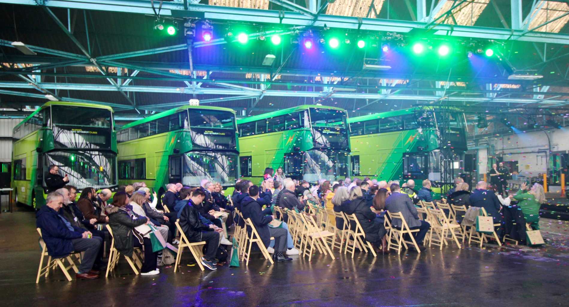 People on fold-out chairs in front of a row of green buses