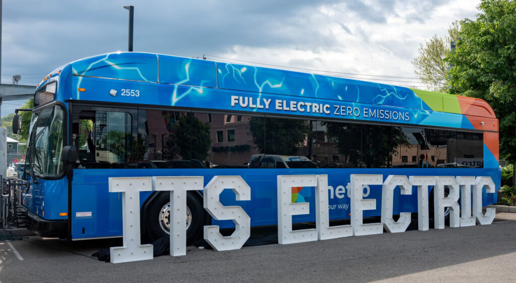 A blue bus in front of a sign that reads ITS ELECTRIC