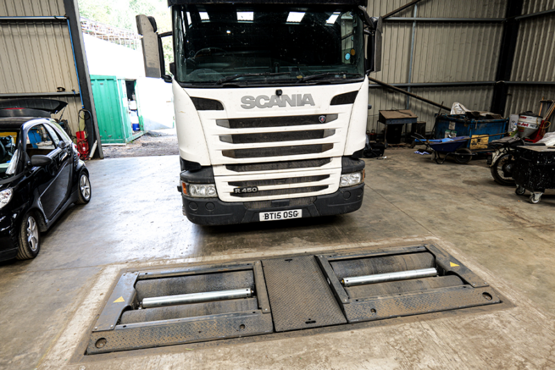 White Scania truck in a workshop in front of a Totalkare in-ground roller brake tester set into the floor