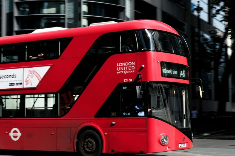 Red London double-decker bus on route 148 to Camberwell Green, with the driver visible in the cab, travelling past glass office buildings
